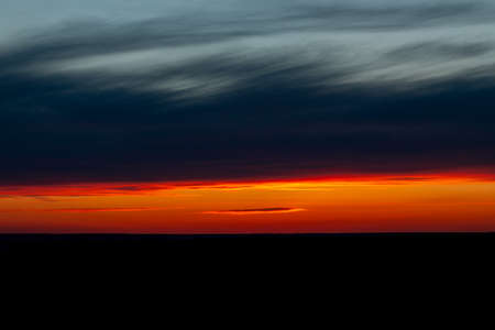Dawn sunrise sunset is located in a stripe in a field on the horizon, the natural background of a beautiful bright colorful dramatic sky with clouds in red-yellow orange tones, with dark stainsの写真素材
