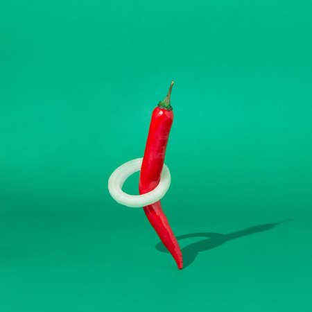 Red hot chili pepper with onion rings on green background. Creative mimimal concept.の写真素材