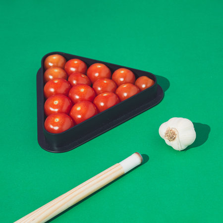 Creative concept made of red cherry tomatoes and biliard cues against vibrant green background.