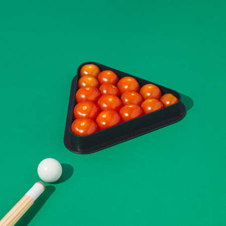 Pool Billiard cues with red cherry tomatoes on a green background.Minimal concept.の写真素材