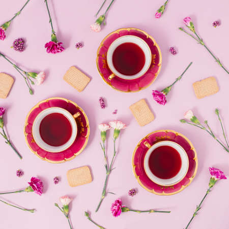 Antique tea cups, flowers and cookies on pink background. Creative minimal concept.  Flat lay.の写真素材
