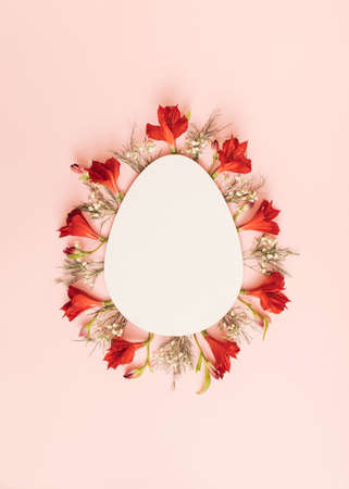 Easter theme with red and white flowers and green leaves. Empty space in the shape of an egg. Minimal spring composition with pastel pink background.の写真素材