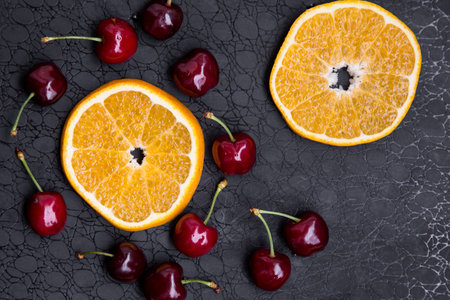 fresh cherries and sliced oranges on a dark background close-up. High quality photo