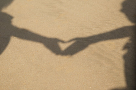 shadows from hands on the sand folded in the shape of a heart