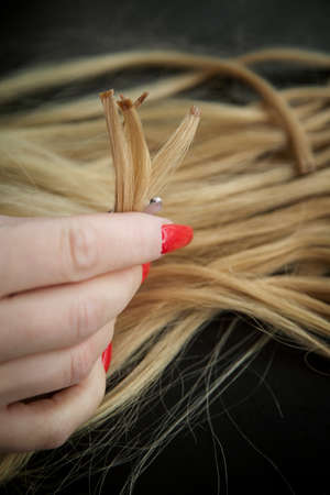 encapsulated strands of blonde hair in womens hands with a bright red manicure. The concept of hair care and extensionの写真素材