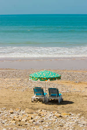 photo of beach chairs and an umbrella on the oceanの写真素材