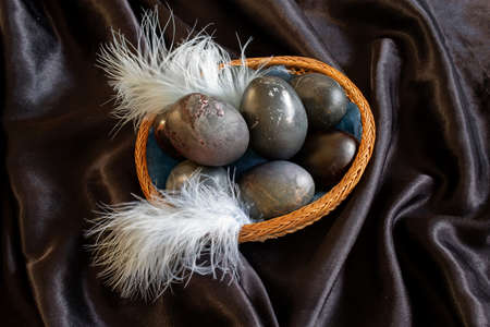 easter-themed photo of black eggs in a wicker plate on a black backgroundの写真素材
