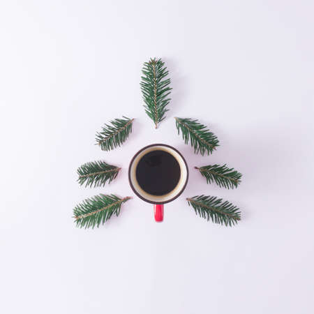 Red mug with coffe and fir branches making christmas tree shape on white background. Winter holiday concept. Minimal New Year flat lay backgroundの写真素材