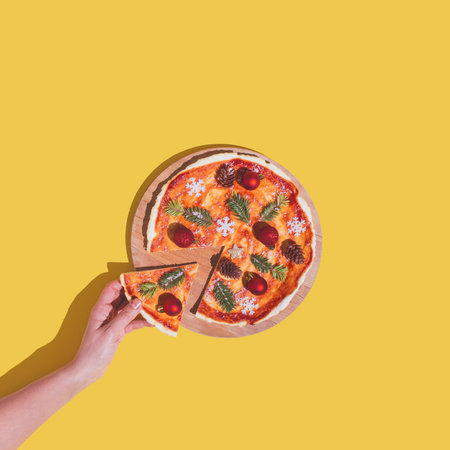 Hand taking piece of pizza with christmas tree decoration as ingredients. New Year flat lay concept...