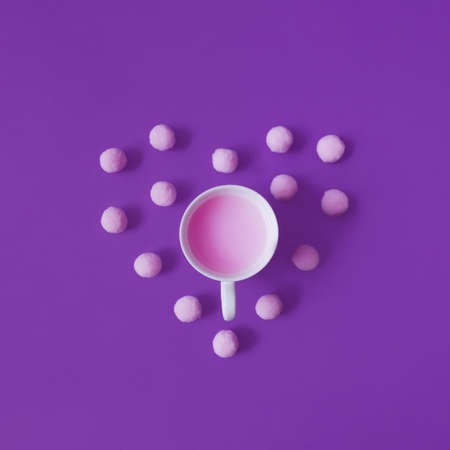 Valentines Day flat lay concept. Cup with pink drink and pink pom poms are making heart shape against violet background.の写真素材