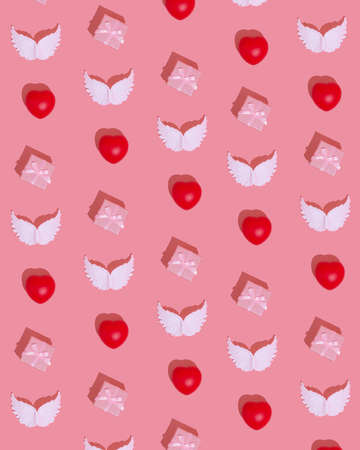 Gift box, white angel wings and red heart are making pattern in minimal flat lay love creative concept. St Valentine's Day romantic creative idea on pink background.の写真素材