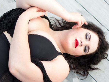 Young beautiful busty curvy  plus size model with big breast in black bra, professional makeup and hairstyle lying on the wooden background, xxl womanの写真素材