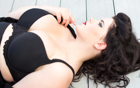 Young beautiful plus size model with big breast in black bra, professional makeup and hairstyle lying on the wooden background, xxl womanの写真素材
