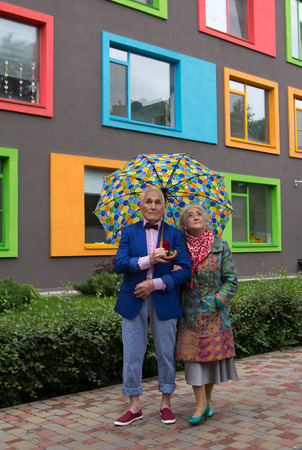 Elegantly dressed old man and an old woman walking under an umbrella in the open air. Woman looks at the sky.の写真素材