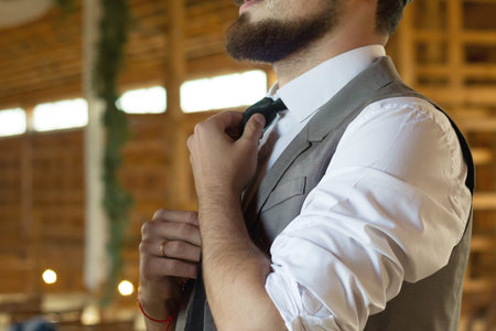 A wedding in a wooden barn. The groom adjusts his tie. Close-up.