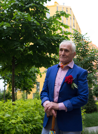 Elegantly dressed old man standing outdoors near the apartment buildings.の写真素材