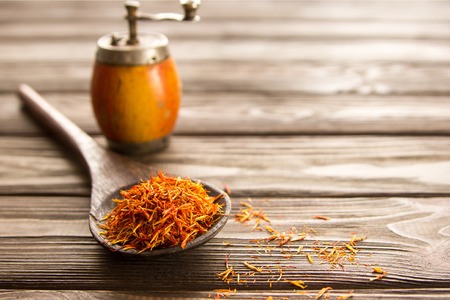 Spice saffron in a wooden spoon on a wooden background,behind a vintage handmill. Close-up.の写真素材