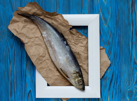 Fish in a frame on a blue wooden table. Herring on paper in a frame. Top view. Vintage.の写真素材