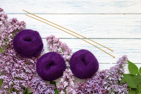 Purple tangles of yarn and knitting needles on a wooden background. Top view. Around the flowers of lilac.の写真素材
