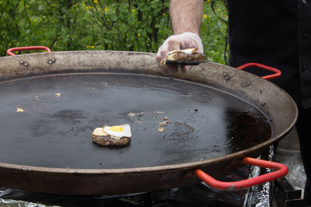 The cook prepares steaks in a huge picnic pan. Outdoors.の写真素材