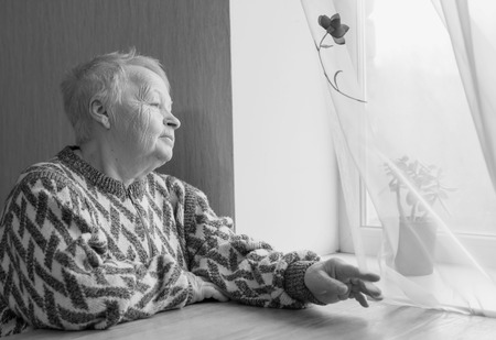 Elderly woman sits and looks out the window. Waiting by the window. Black and white.の写真素材