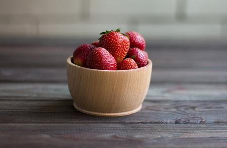 Strawberries in a wooden bowl on a dark wooden table. Close-up.の写真素材