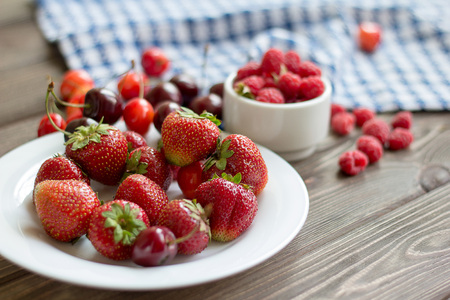 Strawberries, raspberries, cherries in a plate on a wooden table. Close-up.の写真素材