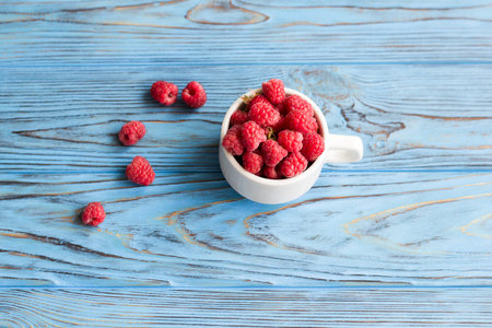 Raspberries in ceramic cup on vintage blue wooden table. Close-up. Top view.