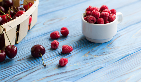 Cherries in basket, raspberries in cup on blue wooden vintage background. Close-up.の写真素材
