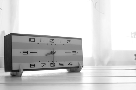 Clock on light wooden table near the window. Morning. Vintage. Black and white.の写真素材