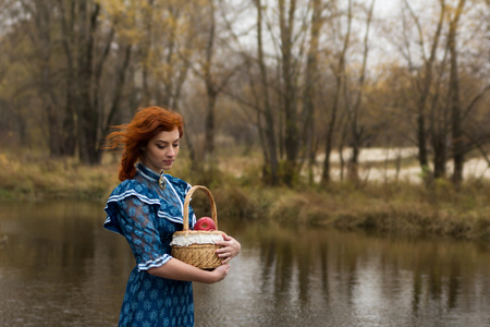 Beautiful young woman holding a basket with apples in autumn in the parkの写真素材