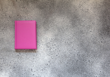 Pink diary on a gray concrete background. Office desktop with pen and pink notebook. Top view.の写真素材