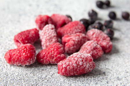 Frozen berries of raspberries and black currant on gray concrete background. Healthy food idea. Top...