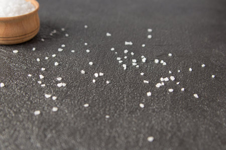 Crystals of salt on a dark cement background. Sea salt in a wooden bowl on a dark concrete...