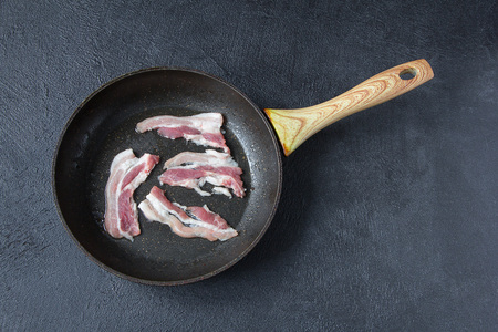 Bacon in a frying pan on a dark stone table. Rustic style. Top view.の写真素材