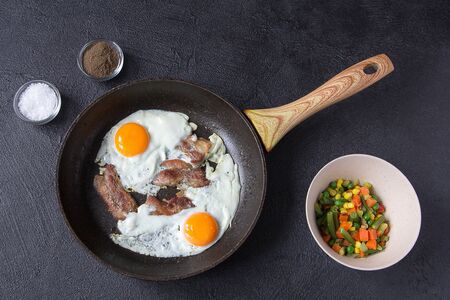 Two fried eggs with bacon and Mexican vegetable mix on dark stone table. Rustic style. Top view.の写真素材