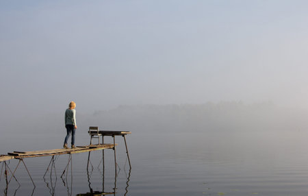 Beautiful young woman on a wooden bridge on the river admiring the sunrise and fog. Beautiful blur...