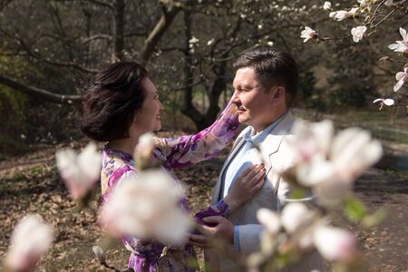 Adult couple walks in the blossoming magnolia garden. Elegant age pair in the garden of magnolias....