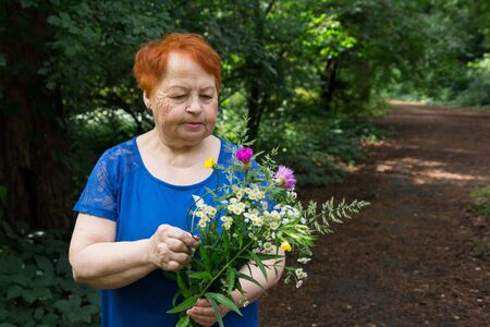 elderly woman in a park is holding a bouquet of flowers collectsの写真素材