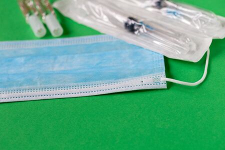 Disposable medical face mask, syringes and injection on a green background.の写真素材
