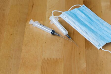 Blue medical disposable face mask and syringes on a wooden table.の写真素材