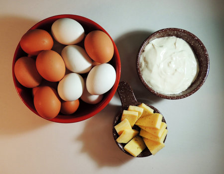 three earthenware bowls with white and brown eggs, sour cream and cheese