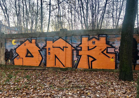 Graffiti in the form of orange letters on a stone wall in an abandoned Park in autumnの写真素材