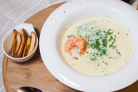 Soup cream shrimp on a white plate on a tree with breadの写真素材