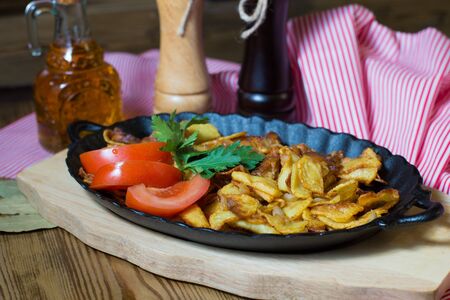 potatoes fried meat in a frying pan on a tree onionの写真素材