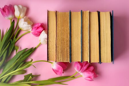 Stack of old books, pink Tulip flowers isolated on a pink background. World book day. Children's reading, children's fantasy. Child's inner world.の写真素材