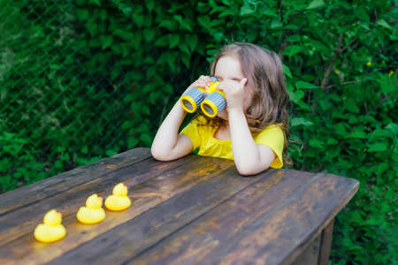 cute little girl playing with rubber duck and plastic binoculars outdoors. beautiful baby having fun with a toy duckling. home development of children. selective focusの写真素材