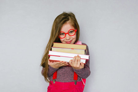 Back to school. Portrait of a blonde schoolgirl in red glasses with a bag and books. Gray Studio...