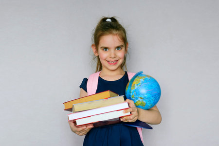 Back to school. Portrait of a fair-haired schoolgirl with a bag and books. Gray Studio background. Education. Smiling at the camera. Copyspace.の写真素材