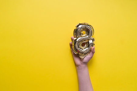 Girl's Kid Hand holds a Golden helium balloon number 8 on a Yellow Background. International Women's Day and March 8の写真素材
